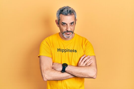 Handsome middle age man with grey hair wearing t shirt with happiness word message skeptic and nervous, disapproving expression on face with crossed arms. negative person.