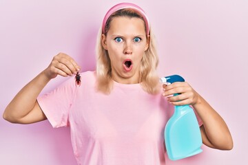 Beautiful caucasian blonde woman holding cockroach and pesticide sprayer afraid and shocked with...
