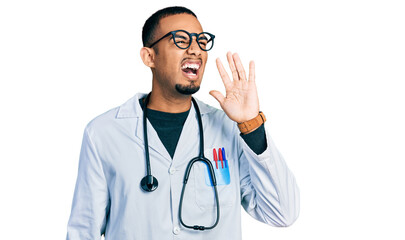 Fototapeta premium Young african american man wearing doctor uniform and stethoscope shouting and screaming loud to side with hand on mouth. communication concept.