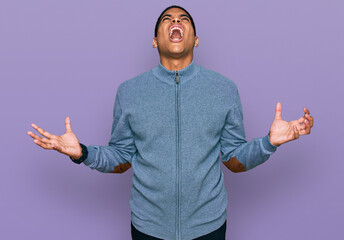 Young handsome hispanic man wearing casual sweatshirt crazy and mad shouting and yelling with aggressive expression and arms raised. frustration concept.