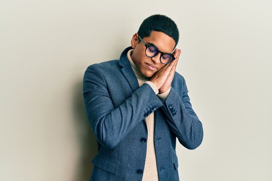 Young handsome hispanic man wearing elegant clothes and glasses sleeping tired dreaming and posing with hands together while smiling with closed eyes.