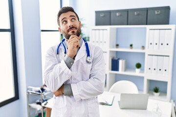 Handsome hispanic man wearing doctor uniform and stethoscope at medical clinic serious face...