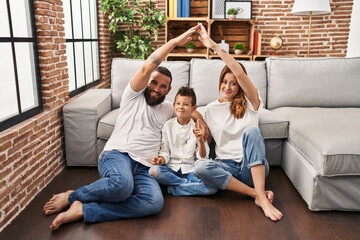 Family of three doing house shape with arms smiling with an idea or question pointing finger with happy face, number one