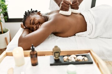 Obraz na płótnie Canvas Young african american woman reciving herbal pouches thai massage at beauty center.