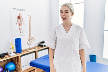 Young caucasian woman working at pain recovery clinic winking looking at the camera with sexy expression, cheerful and happy face.