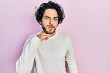 Handsome hispanic man wearing casual white sweater cutting throat with hand as knife, threaten aggression with furious violence