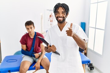 Obraz premium Young hispanic man working at pain recovery clinic with a man with broken arm pointing fingers to camera with happy and funny face. good energy and vibes.