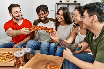 Group of young friends smiling happy eating italian pizza sitting on the sofa at home.