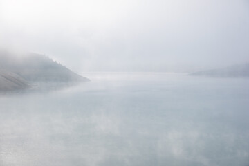 Soft, abstract, minimalist, misty view of an evaporating lake on a foggy morning with a lot of copy space