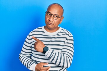 Middle age latin man wearing casual clothes and glasses pointing with hand finger to the side showing advertisement, serious and calm face