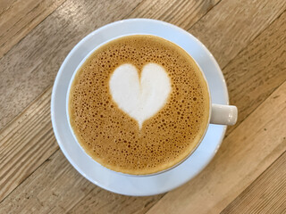 A mug of flat white or latte art coffee on a wooden background. Coffee art. Heart flower shape latte art