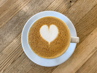 A mug of flat white or latte art coffee on a wooden background. Coffee art. Heart flower shape latte art