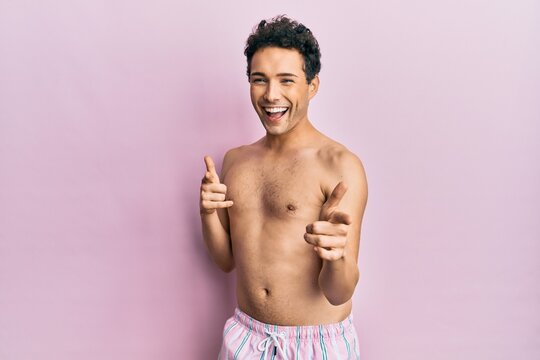 Young handsome man wearing swimwear shirtless pointing fingers to camera with happy and funny face. good energy and vibes.