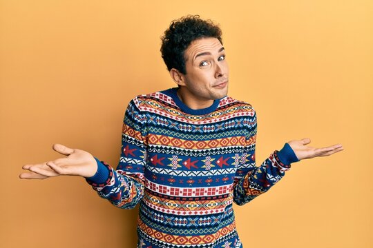 Young handsome man wearing casual winter sweater clueless and confused expression with arms and hands raised. doubt concept.