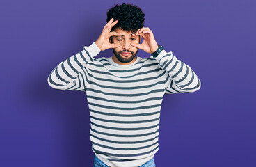 Young arab man with beard wearing casual striped sweater trying to open eyes with fingers, sleepy and tired for morning fatigue