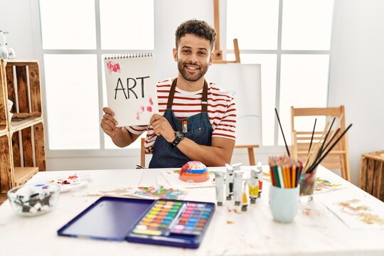 Young arab artist man smiling happy holding notebook with art word at art studio.