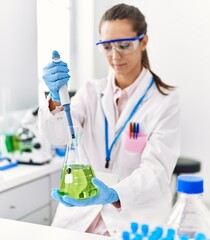 Young hispanic woman wearing scientist uniform using pipette and test tube working at laboratory