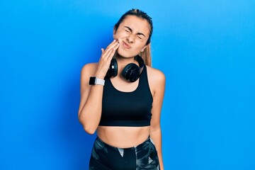 Fototapeta na wymiar Beautiful hispanic woman wearing gym clothes and using headphones touching mouth with hand with painful expression because of toothache or dental illness on teeth. dentist