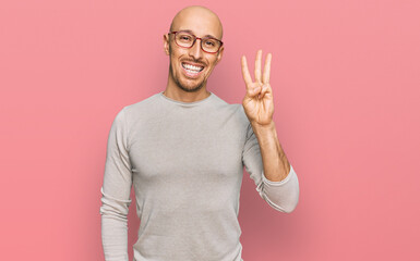 Naklejka premium Bald man with beard wearing casual clothes and glasses showing and pointing up with fingers number three while smiling confident and happy.
