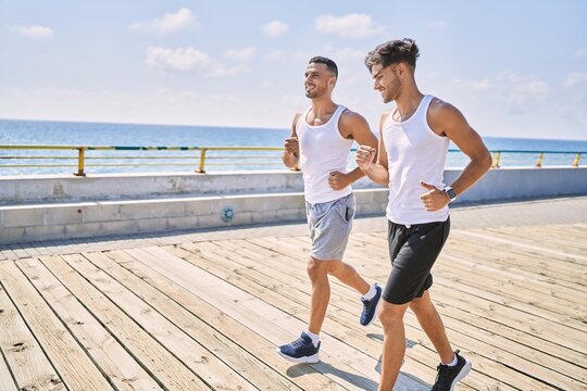 Two hispanic men sporty couple smiling confident running at seaside