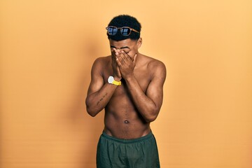 Young african american man wearing swimwear and swimmer glasses with sad expression covering face...