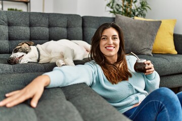 Young woman drinking mate infusion sitting with dog at home