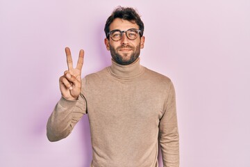 Handsome man with beard wearing turtleneck sweater and glasses showing and pointing up with fingers...