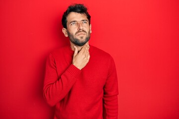 Handsome man with beard wearing casual red sweater touching painful neck, sore throat for flu, clod and infection