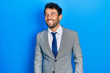 Handsome man with beard wearing business suit and tie looking away to side with smile on face, natural expression. laughing confident.