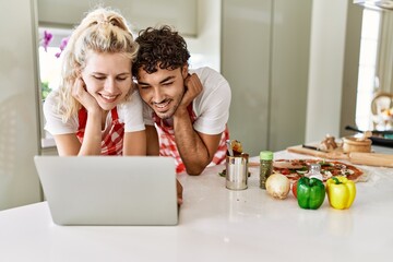 Young couple smiling happy using laptop at kitchen.