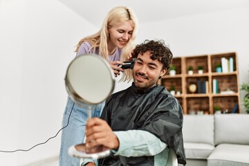 Young woman cutting hair to her boyfriend at home.