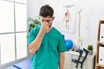 Fototapeta premium Young man with beard working at pain recovery clinic tired rubbing nose and eyes feeling fatigue and headache. stress and frustration concept.