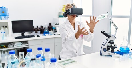 Middle age blonde woman wearing scientist uniform using vr goggles working at laboratory