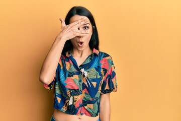 Young hispanic woman wearing casual clothes peeking in shock covering face and eyes with hand, looking through fingers afraid