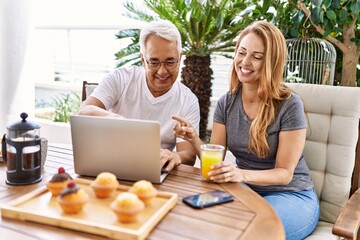 Middle age hispanic couple having breakfast using laptop at the terrace.