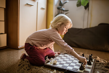 child plays single game of chess at home on floor. Chessboard with the end of the game of chess. Learning to play chess for kids. Chess pieces on the sunlit board of the house on floor