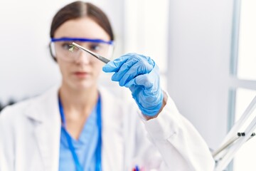 Young hispanic woman wearing scientist uniform holding insect with tweezers at laboratory