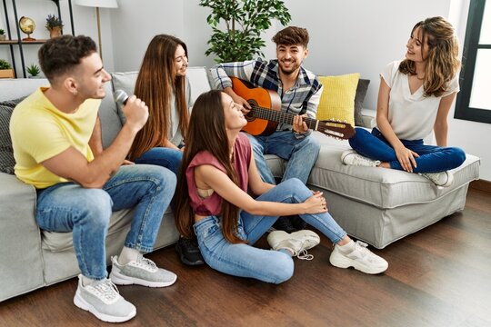 Group of young friends on party playing classical guitar and singing song at home.