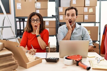 Middle age couple working at small business ecommerce afraid and shocked, surprise and amazed...