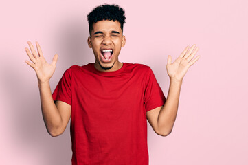 Young african american man wearing casual red t shirt celebrating mad and crazy for success with arms raised and closed eyes screaming excited. winner concept