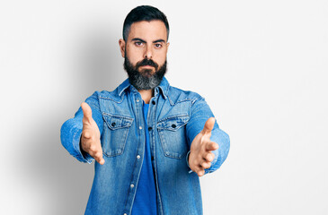 Hispanic man with beard with open arms doing hug gesture relaxed with serious expression on face....