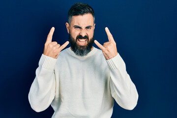 Young hispanic man wearing casual clothes shouting with crazy expression doing rock symbol with...