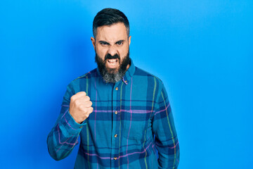 Young hispanic man wearing casual clothes angry and mad raising fist frustrated and furious while...