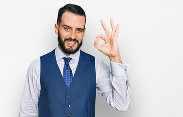 Young man with beard wearing business vest smiling positive doing ok sign with hand and fingers. successful expression.