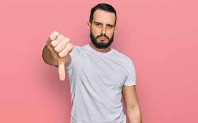 Young man with beard wearing casual white t shirt looking unhappy and angry showing rejection and...