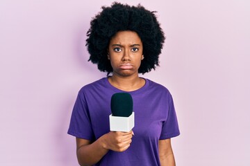 Fototapeta na wymiar Young african american woman holding reporter microphone skeptic and nervous, frowning upset because of problem. negative person.