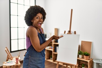 Young african american woman with afro hair at art studio pointing aside with hands open palms showing copy space, presenting advertisement smiling excited happy