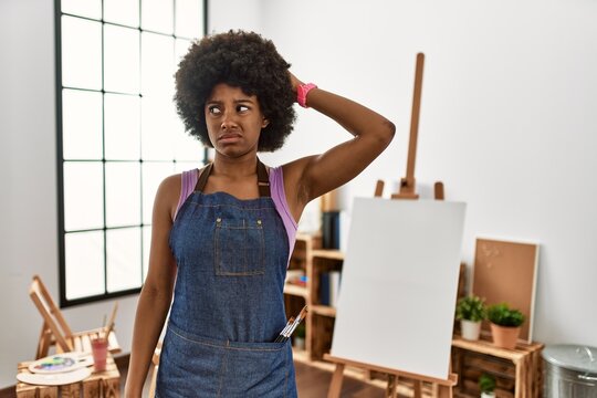 Young african american woman with afro hair at art studio confuse and wondering about question. uncertain with doubt, thinking with hand on head. pensive concept.