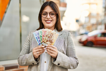 Young hispanic businesswoman smiling happy holding canandian dollars at the city.