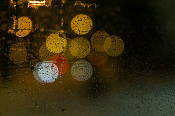 blurred colored street lights from wet car's front window. water drops on the glass.